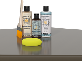 Retique It Black Walnut Kit with Gloss Tripletique, Light Wood Wood'n Primer, Black Walnut Gel Stain Alternative, paintbrush, and yellow sponge on a tabletop.