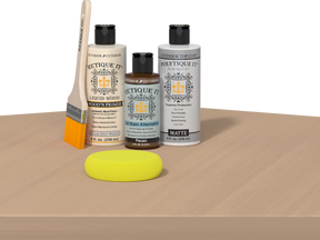 Retique It® Pecan Multipurpose Kit contents with Bleached Wood Liquid Wood primer, Pecan gel stain alternative, PolyTique It® matte exterior top coat, paintbrush, and yellow sponge displayed on a light wood surface.