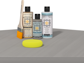Retique It® Weathered Wood Multipurpose Kit contents with Light Wood Liquid Wood primer, Weathered Wood gel stain alternative, Tripletique matte interior top coat, paintbrush, and yellow sponge displayed on a wood surface.