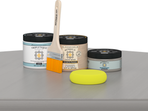 Retique It® Weathered Wood Multipurpose Kit contents with Liquid Wood primer, Weathered Wood gel stain alternative, Tripletique satin interior top coat, paintbrush, and yellow sponge displayed on a gray wood surface.