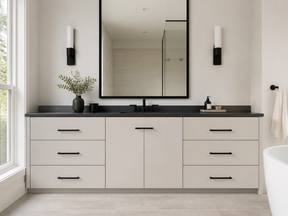 Modern bathroom with a light neutral vanity, black countertop, black hardware and fixtures, large black-framed mirror, wall sconces, greenery, and a glass-enclosed shower.